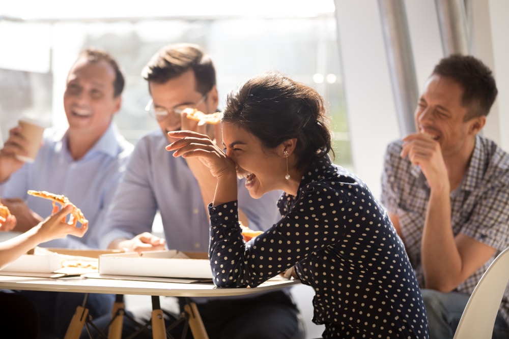 group of people laughing around a table with pizza